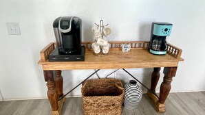 A wooden coffee table with two coffee makers, a mug holder, and a wicker basket. - The Wave Cave by Silver Sands Vacation Rentals (Port Aransas)