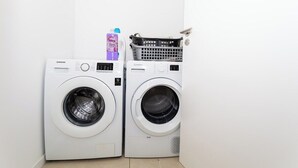 Two white front-loading washing machines with a basket and a bottle of laundry detergent on top. - GuestReady - GuestHouse Passal - S. Miguel (Ponta Delgada)