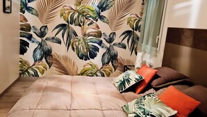 Ein Schlafzimmer mit einem Bett, Kissen und einer Wand mit tropischem Blattmuster.