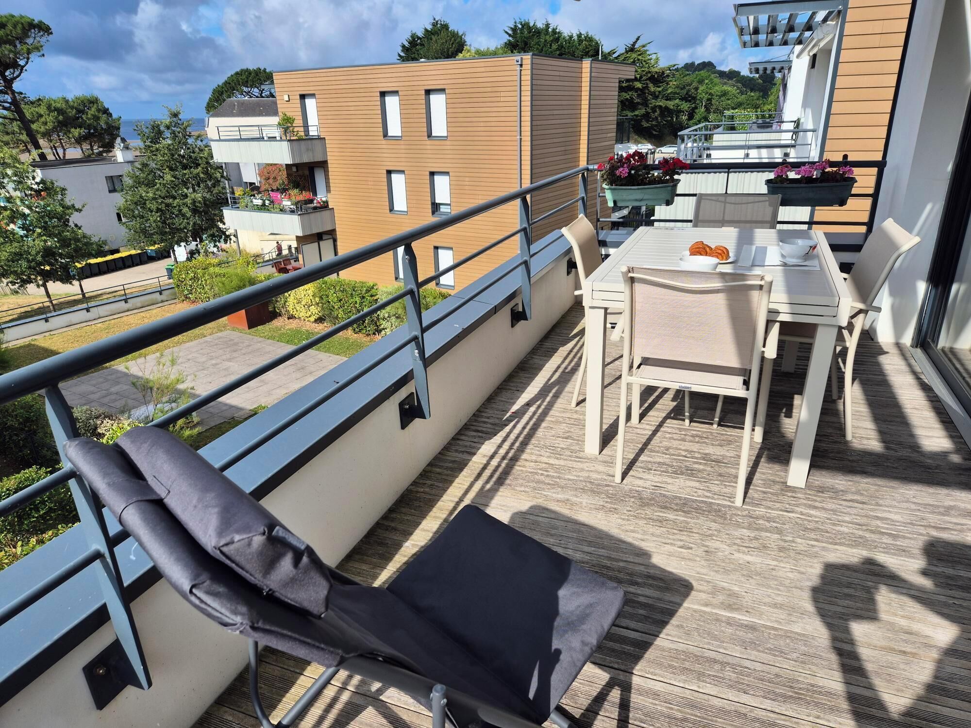 Un balcon avec une table et des chaises, un fauteuil confortable et une vue sur les bâtiments et la verdure.