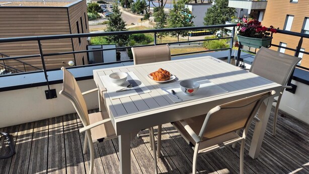 Ein Balkon mit einem Tisch für zwei Personen, einer Schüssel, einem Löffel und einem Croissant.