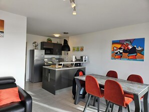 Cozinha moderna com ilha central, mesa de jantar com cadeiras e um sofá preto.