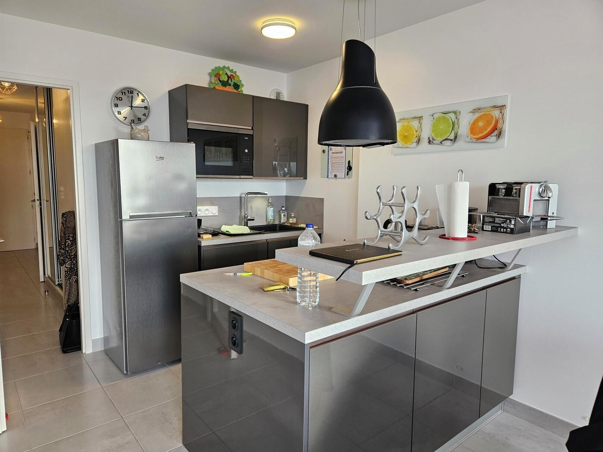 Uma cozinha moderna com ilha central, eletrodomésticos de aço inoxidável e luminária pendente.