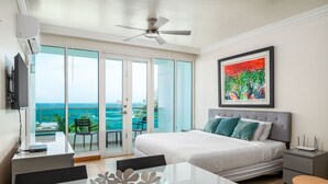 Een moderne hotelkamer met een groot bed, een bureau, een eettafel en een balkon met uitzicht op de oceaan.