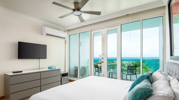 Een slaapkamer met een bed, een televisie, een dressoir en een balkon met uitzicht op zee.