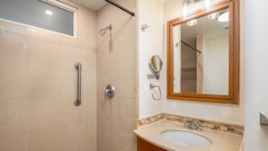 Een badkamer met douche, handgreep, wastafel en spiegel.