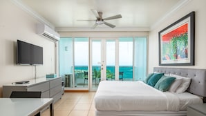Een hotelkamer met een bed, een bureau, een televisie en een balkon met uitzicht op zee.