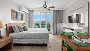 Habitación de hotel con cama, escritorio, silla, televisión y balcón con vista a la ciudad.