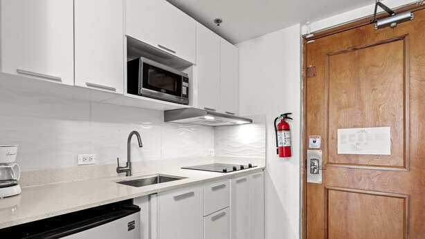 A modern kitchen with white cabinetry, a stainless steel sink, a microwave, and a fire extinguisher.