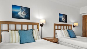 A hotel room with two beds, each with a wooden headboard, white bedding, and a nightstand with a lamp. There are two paintings on the wall above the beds.