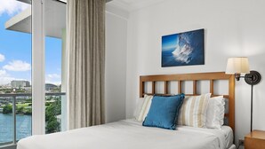 A hotel room with a bed, a view of a body of water, and a painting on the wall.