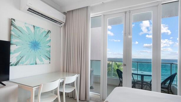 A hotel room with a balcony, a desk with chairs, a bed, and a large window with a view of the sea. - Oceanfront Old San Juan Panoramic Balcony (San Juan)