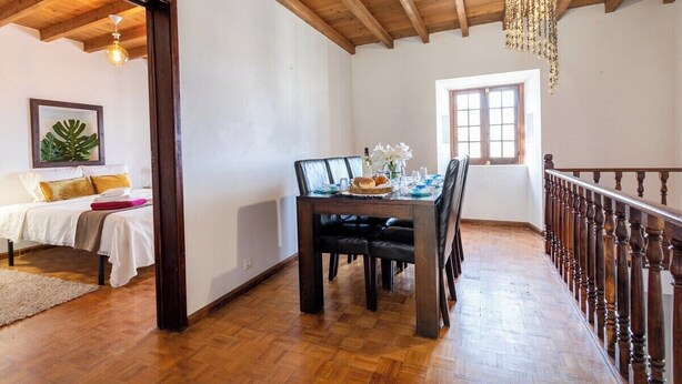 Une pièce avec un plafond en bois, une table à manger dressée avec des assiettes, des verres et un centre de table, et un lit recouvert d’une couette blanche et agrémenté d’oreillers.