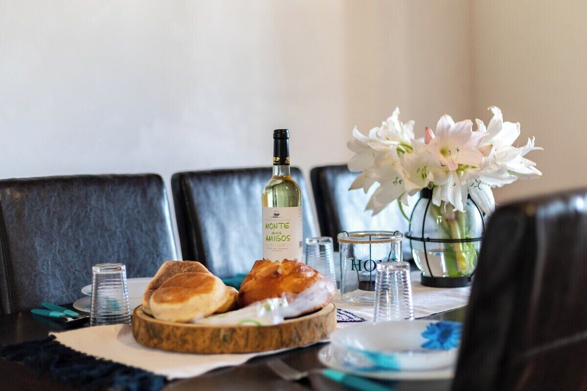 A dining table with a bottle of wine, a vase of flowers, and a plate with bread.