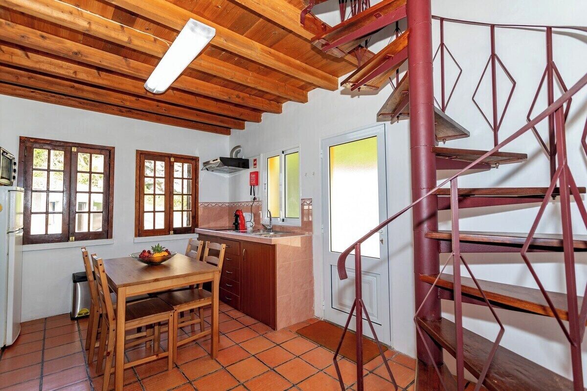 Een keuken met houten balken, een eettafel, stoelen, een rode spiraaltrap en een raam met uitzicht.