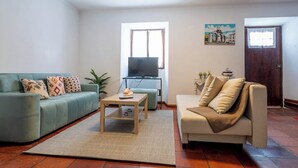 Un salon avec un canapé vert, un canapé beige, une table basse et un téléviseur.