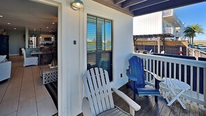 A covered porch with Adirondack chairs, a dining area with a table and chairs, and a view of the ocean and buildings. - Sugar Shack by Silver Sands Vacation Rentals (Port Aransas)