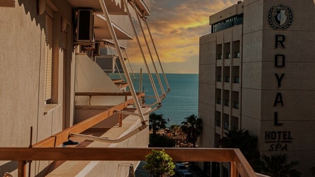 A balcony with a wooden table and chairs, overlooking a hotel building and the sea. - Lovely 2-bedroom apartment with sea view in Durrës (Durrës)