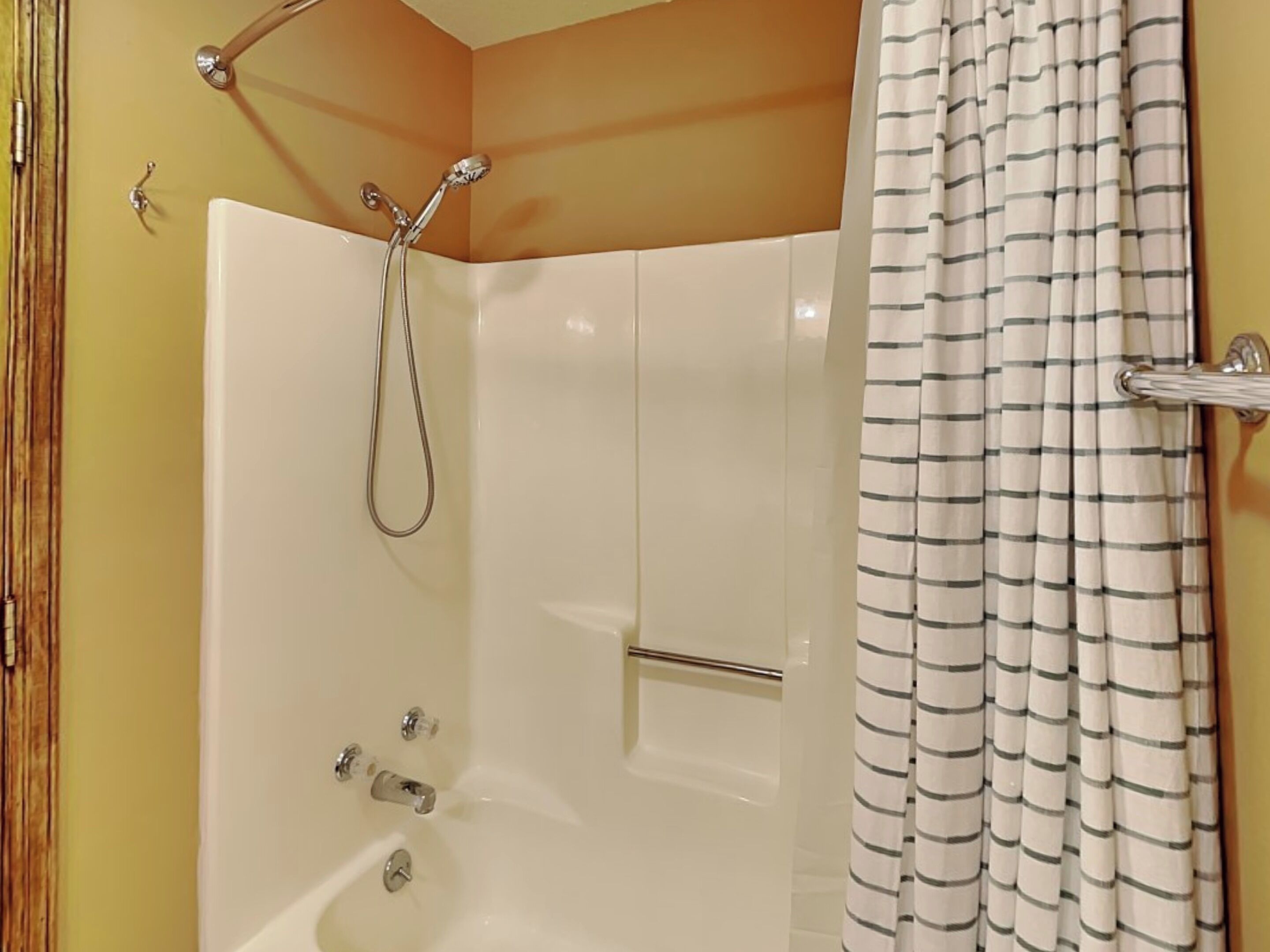 A bathroom with a bathtub, shower, and a striped shower curtain.