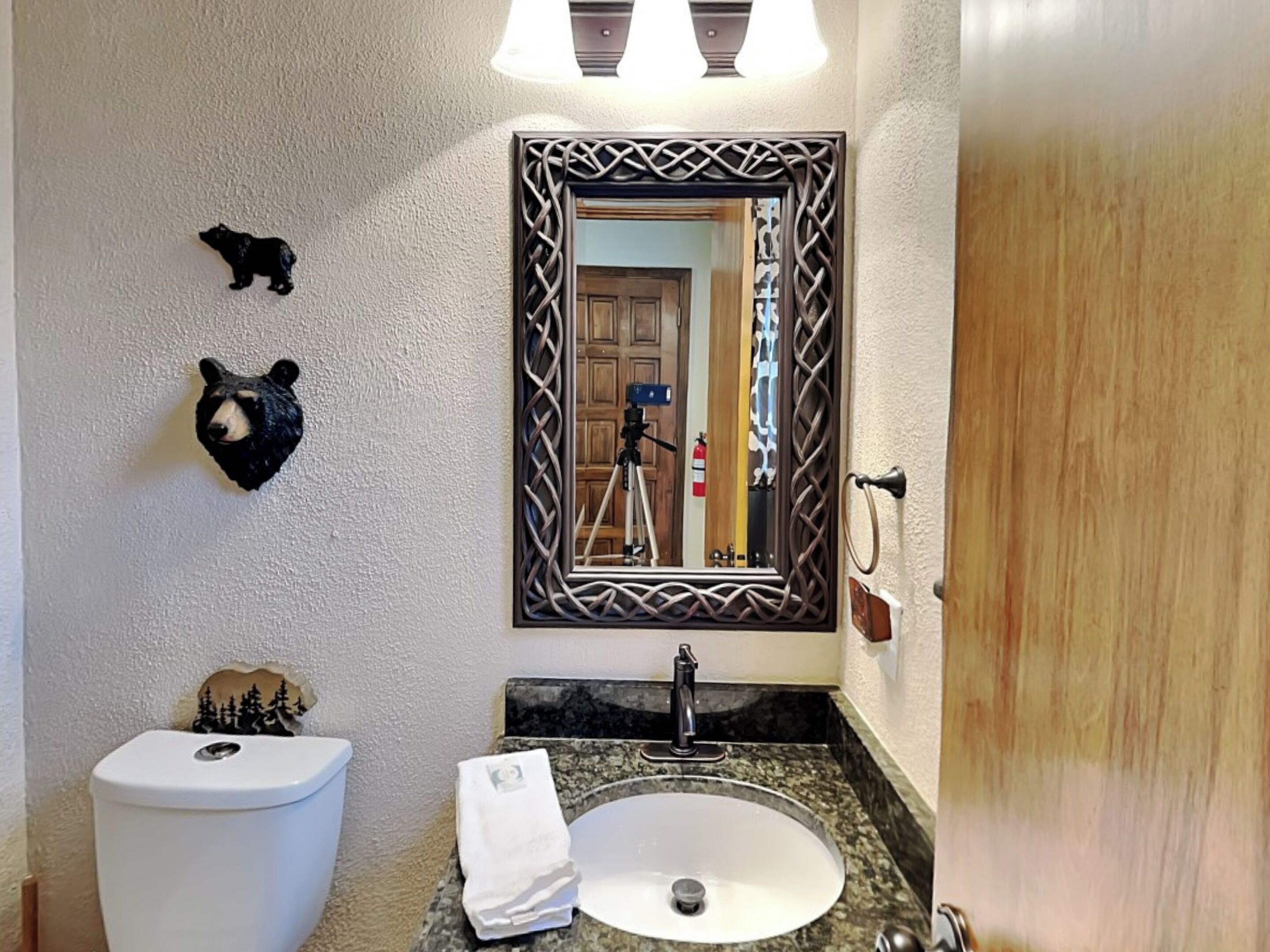 A bathroom with a toilet, sink, and mirror. There are bear head decorations on the wall.