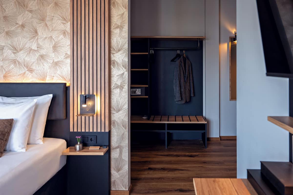 Une chambre d’hôtel moderne équipée d’un lit, d’une table de chevet, d’une petite table et d’une armoire intégrée avec un banc.