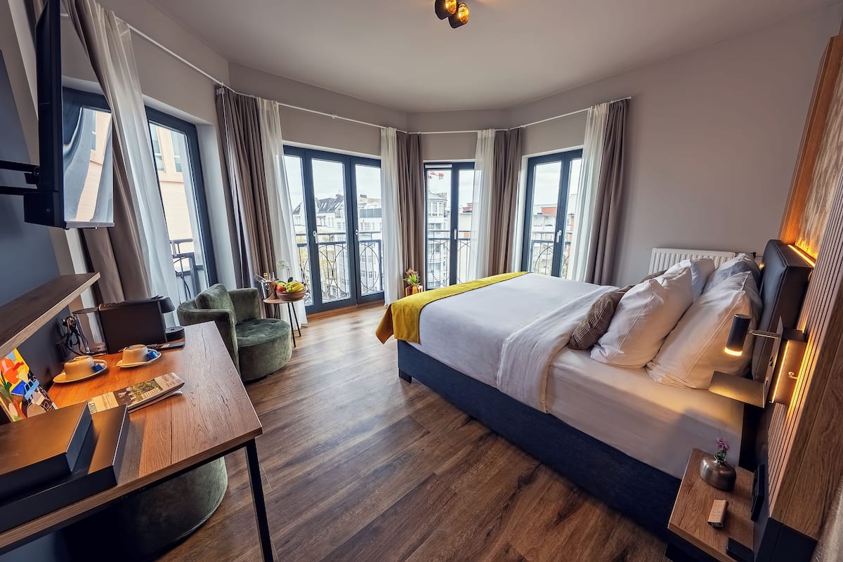 Une chambre d’hôtel avec un lit, un bureau, une chaise et de grandes fenêtres.