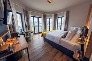 A hotel room with a bed, a desk, a chair, a TV, and large windows. - Residency NO7 (Berlin)