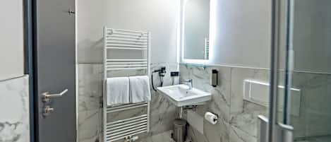 A modern bathroom with a glass shower enclosure, a white sink, and a marble-tiled floor.