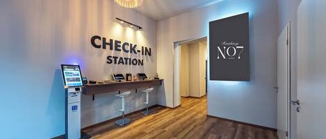 A check-in station with a digital kiosk, bar stools, and a chandelier.