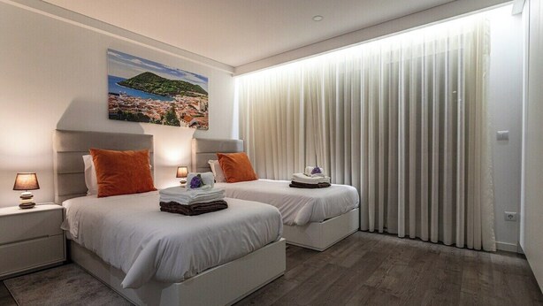 Een moderne hotelkamer met twee bedden, een groot raam met dunne gordijnen, een schilderij aan de muur en een houten vloer.