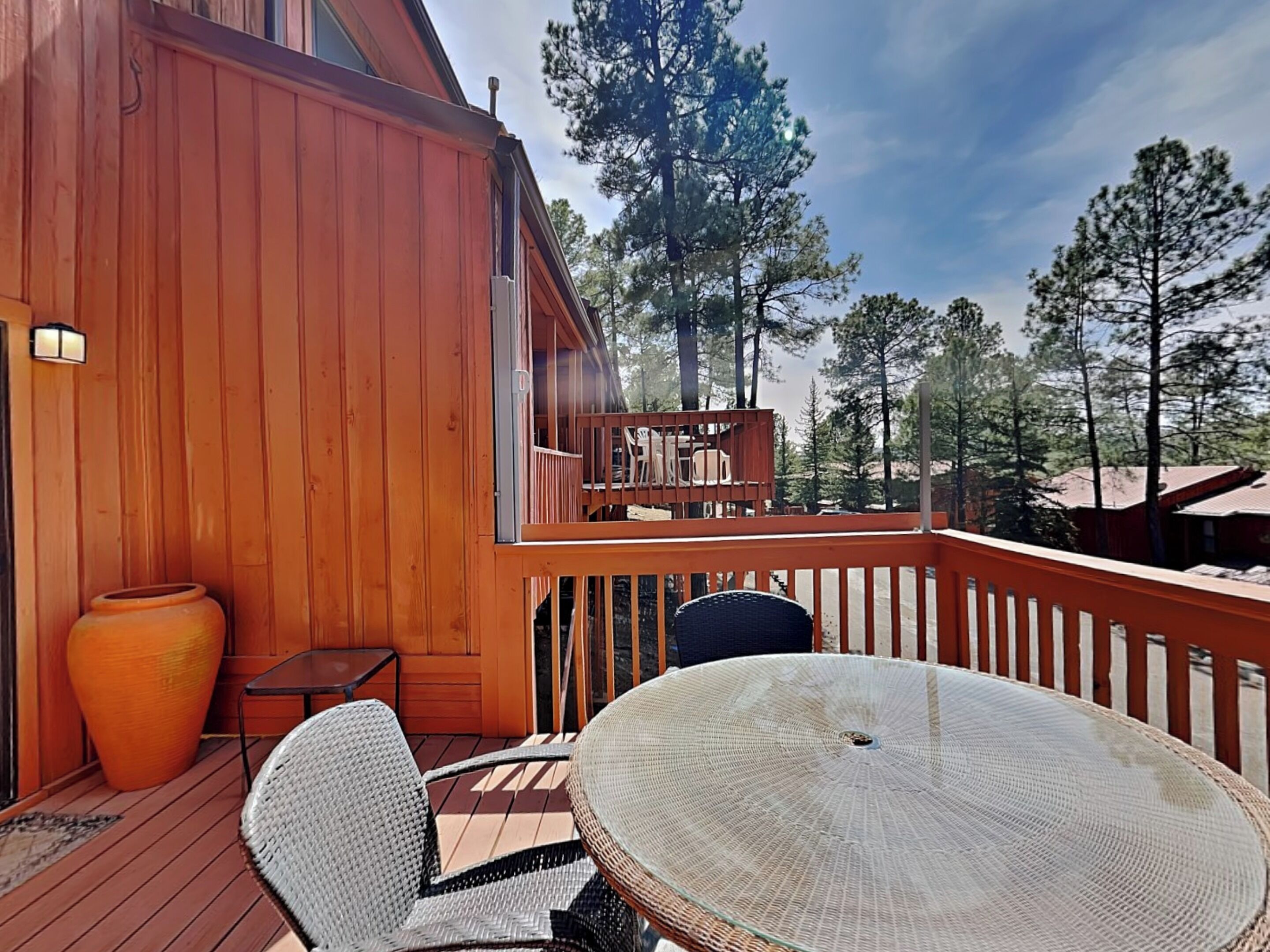 Een houten terras met een ronde tafel en twee stoelen, een grote vaas en een bijzettafeltje.
