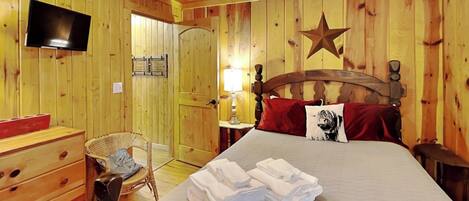 A wooden-paneled room with a bed, a television, a star decoration, and a ceiling fan.