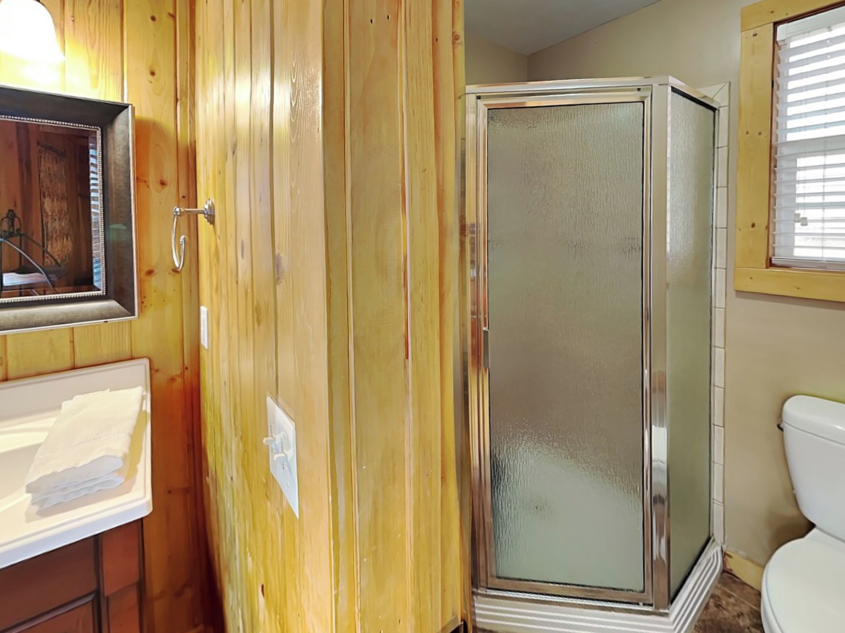 A bathroom with wooden paneling, a glass shower enclosure, a white sink, and a toilet.