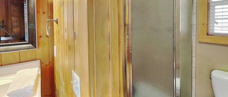 A bathroom with wooden paneling, a glass shower enclosure, a white sink, and a toilet.