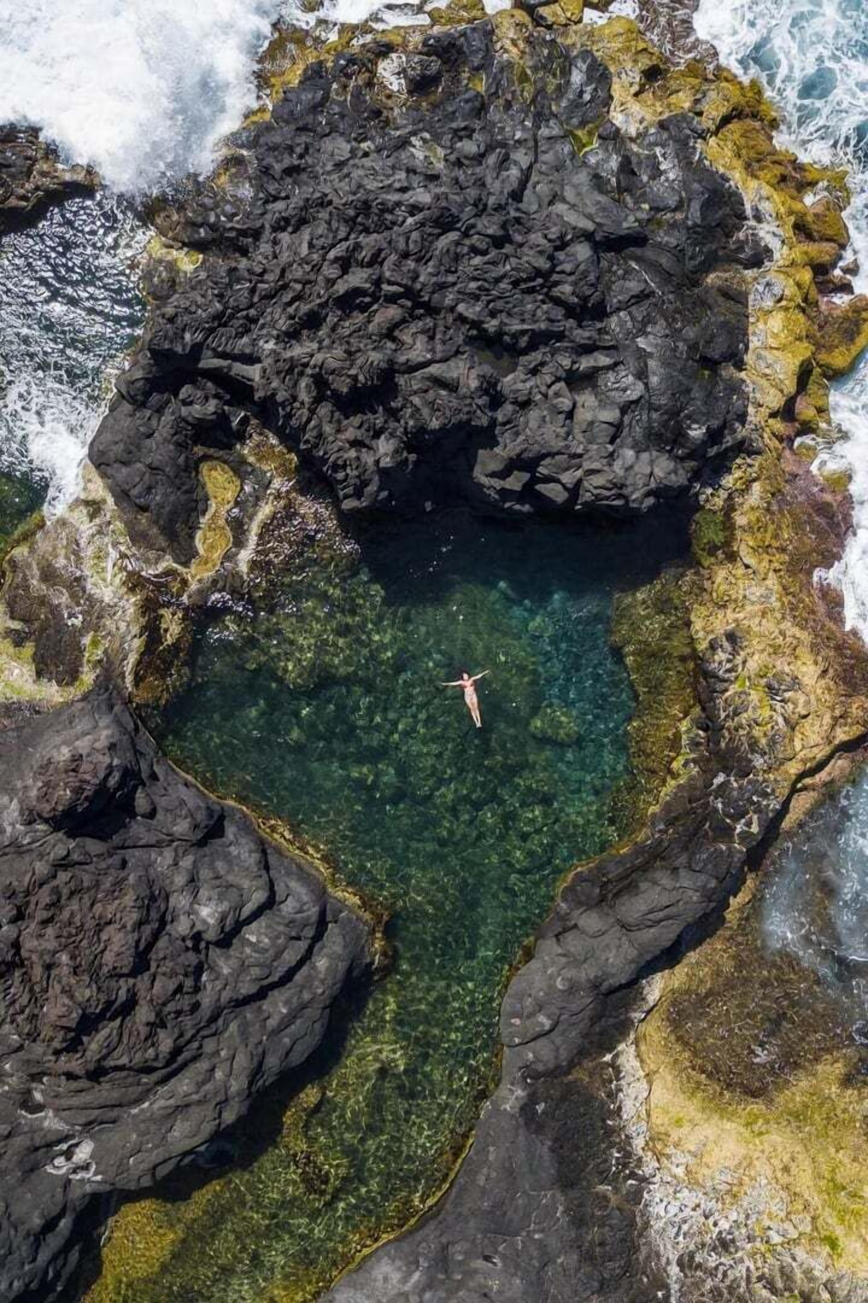 A person swimming in a natural pool surrounded by rocky terrain.