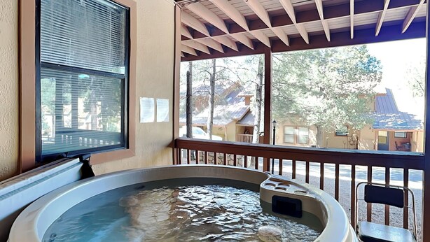 A hot tub on a wooden deck with a view of houses and trees. - Pinon Park A15 by Ruidoso Vacation Rentals (Ruidoso)
