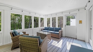 A covered porch with wicker furniture, large windows, and a door.