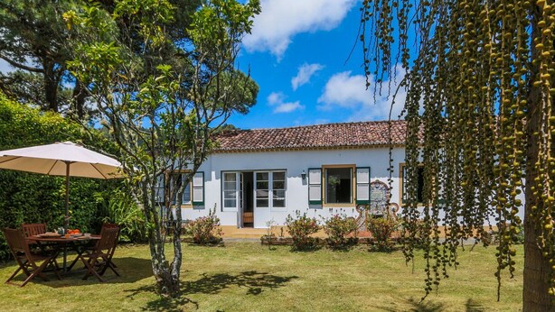 A house with a tiled roof, a front door, and a small garden with a table and chairs.