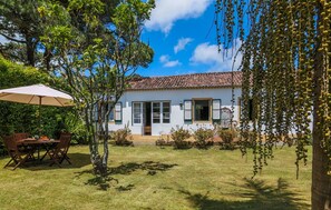 Una casa con tejado de baldosas, una puerta principal y un pequeño jardín con una mesa y sillas.