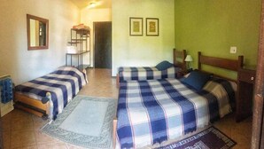 Een kamer met twee bedden, een tafeltje, een stoel en een plank met opgevouwen kleding.