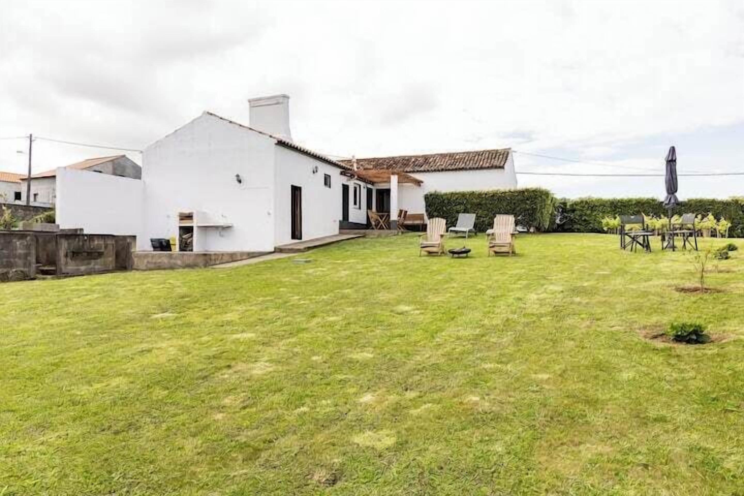 Una casa bianca con tetto in tegole, un piccolo giardino antistante e posti a sedere all'aperto.