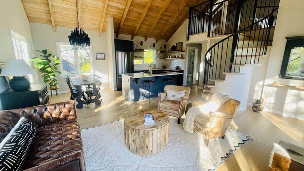 A spacious living area with a wooden ceiling, a sofa, a coffee table, and a kitchen in the background.