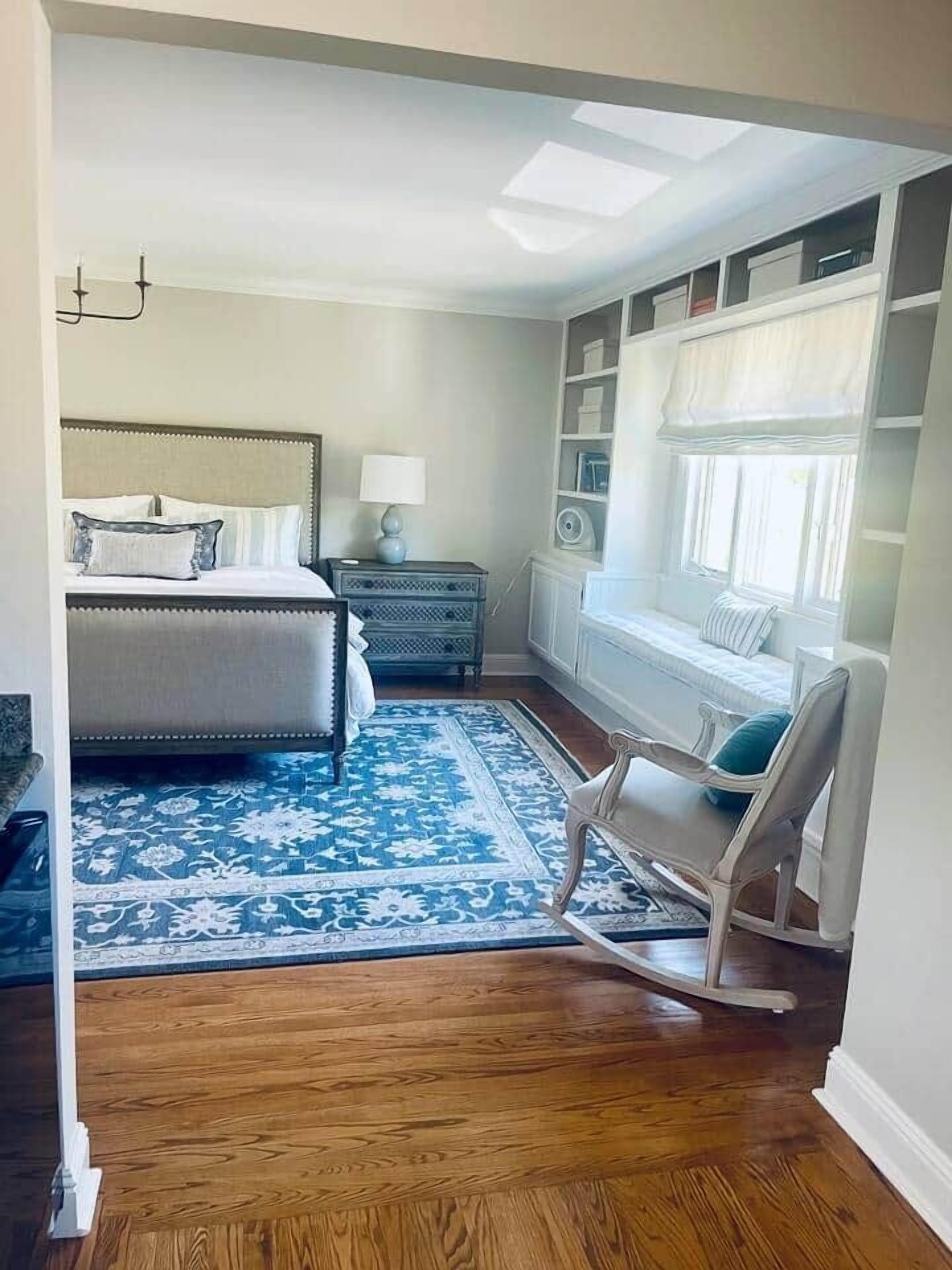 A bedroom with a bed, nightstand, lamp, chair, and a window with a view.