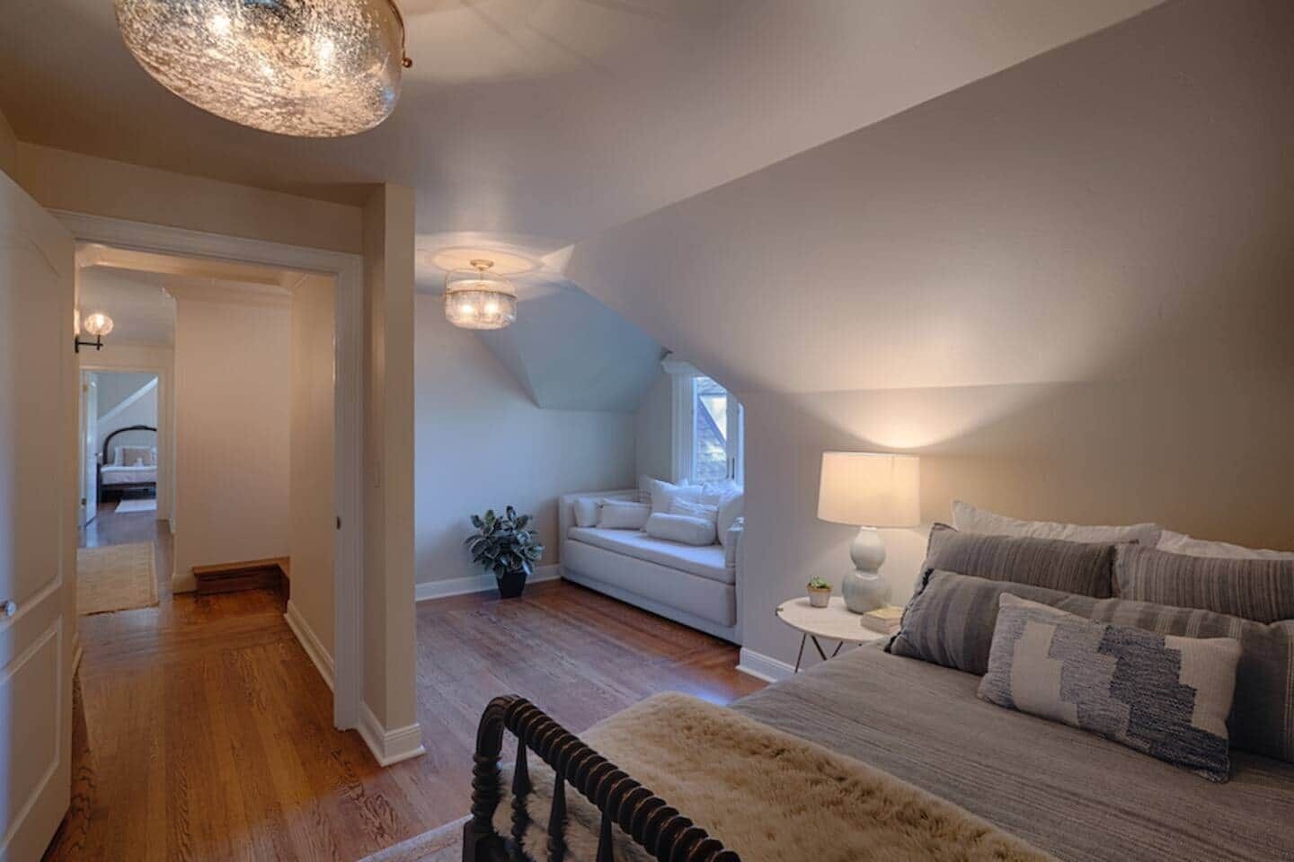 Une chambre à coucher avec un grand lit, une petite table de chevet, une lampe, une fenêtre et un luminaire au plafond.
