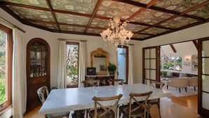 Une salle à manger avec une grande table, des chaises en bois, un lustre et un plafond orné de motifs floraux.