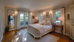 Une chambre spacieuse avec un grand lit, un plancher en bois, un balcon et une vue sur l’extérieur.