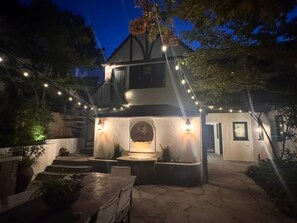 A two-story building with a stone facade, a central courtyard with steps leading to a seating area, and string lights. - Timeless Elegance-5BR 1930s Home (Sebastopol)