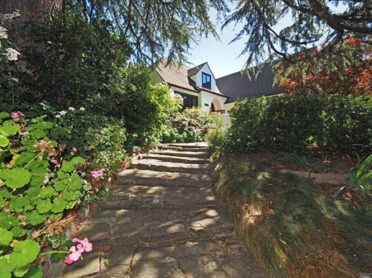 A stone staircase leading to a house surrounded by lush greenery and flowering plants.