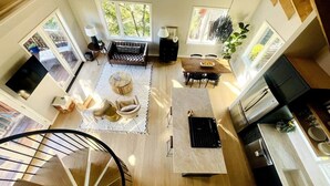 A spacious living area with a staircase, a dining table with chairs, a kitchen area, and large windows providing natural light. - Luxe Guest Home *Walk to Downtown Sebastopol (Sebastopol)