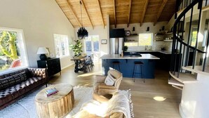 A spacious living area with a wooden ceiling, a sofa, a coffee table, and a chair. A kitchen with a bar and a dining area with chairs and a table are visible in the background. - Luxe Guest Home *Walk to Downtown Sebastopol (Sebastopol)